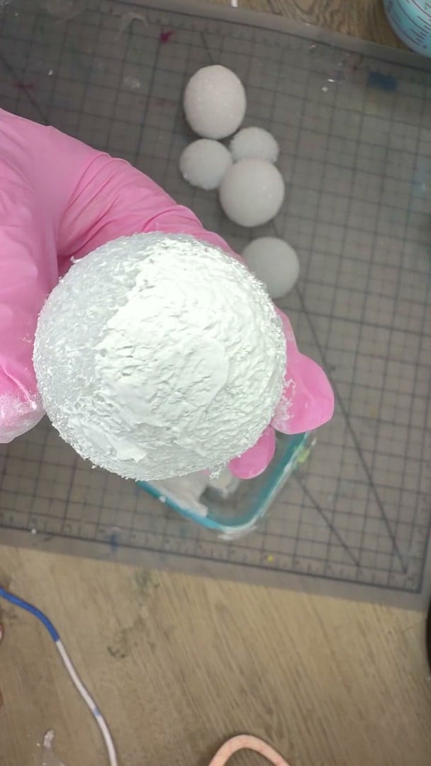 Studio process clip: a pink-gloved hand coating a white textured sphere, more finished white spheres resting on the cutting mat