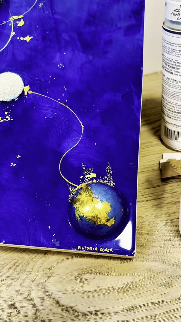 Studio process clip: the cobalt Origin / Inheritance panel upright on a table, a resin sphere filled with gold leaf trailing a gold filament, signed Victoria Zeder
