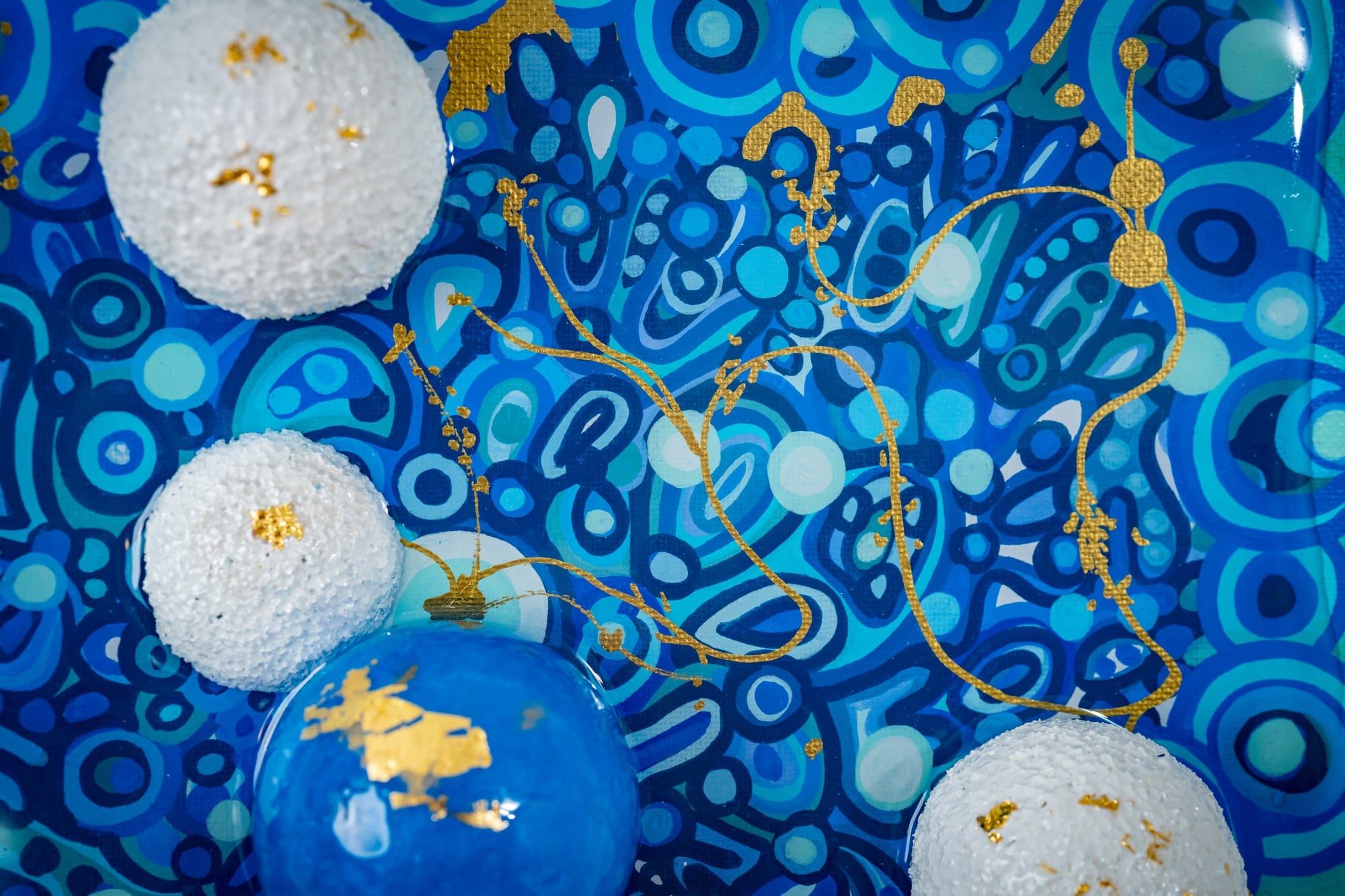 Macro detail of Genesis surface showing hand-carved spheres bound by gold filament under resin