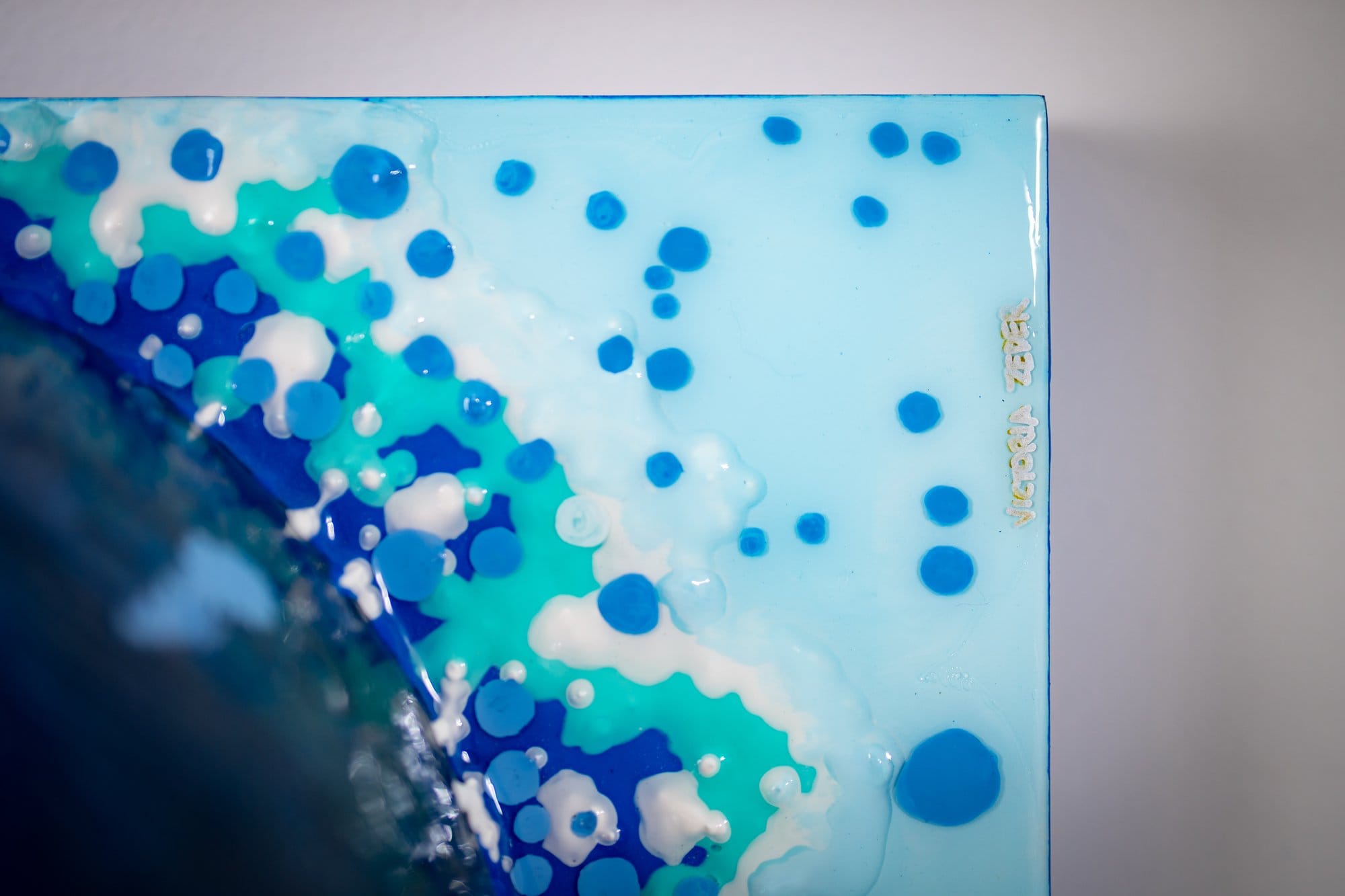 Macro of Eye Sea All I: the signed cerulean resin corner scattered with blue dots, the dark encaustic dome entering at the left edge