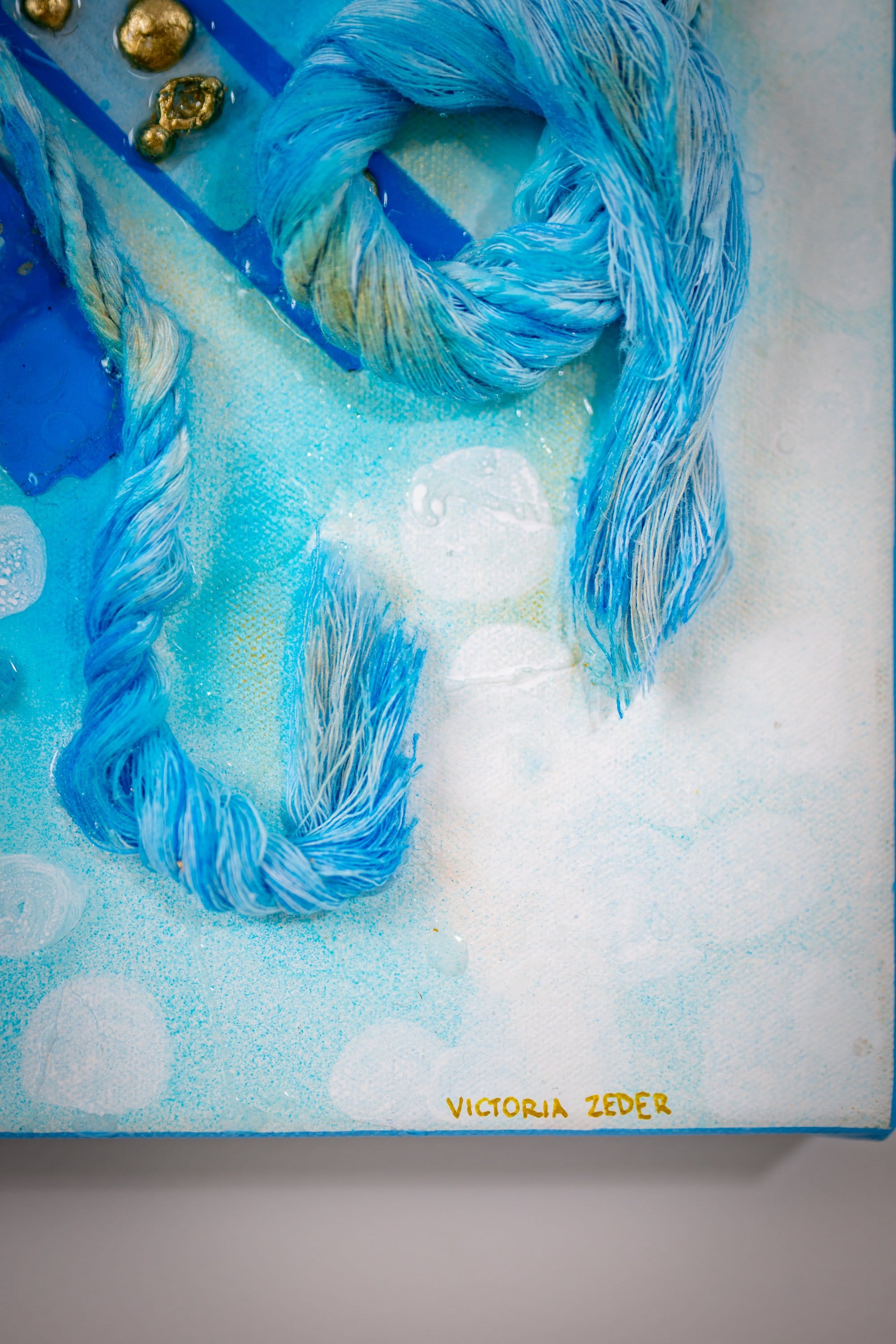 Macro corner of Faceless Self Portrait: twisted blue yarn tentacle coils on a pale dotted cerulean field, gold nuggets and the artist's signature