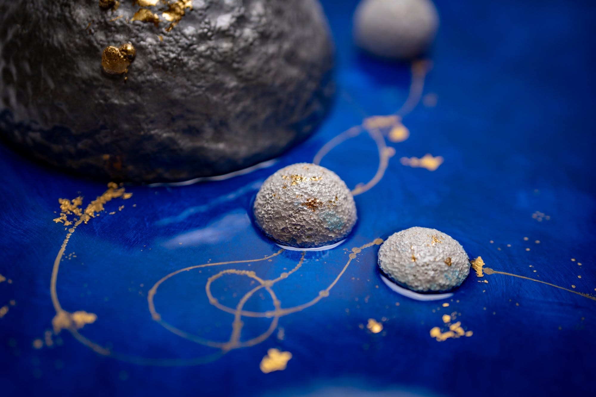 Macro detail of Origin / Inheritance I showing silver hero sphere and satellites in cobalt field