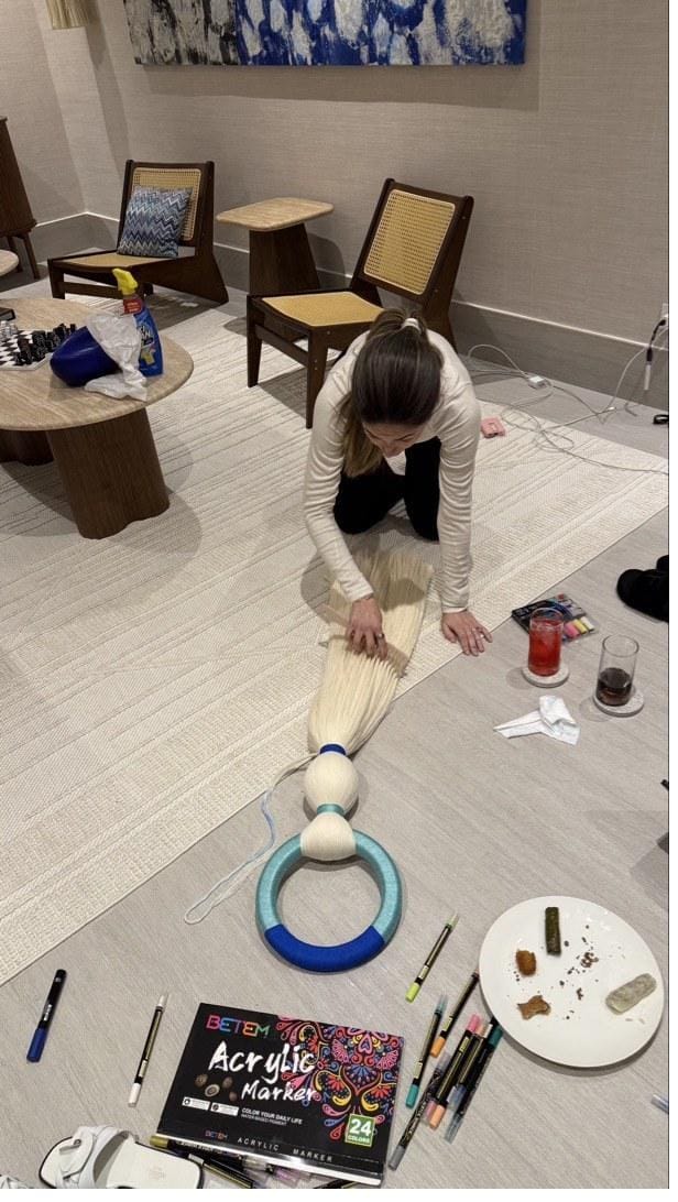 Overhead view of Victoria sitting on the studio rug working on a fiber sculpture project surrounded by art supplies and drinks