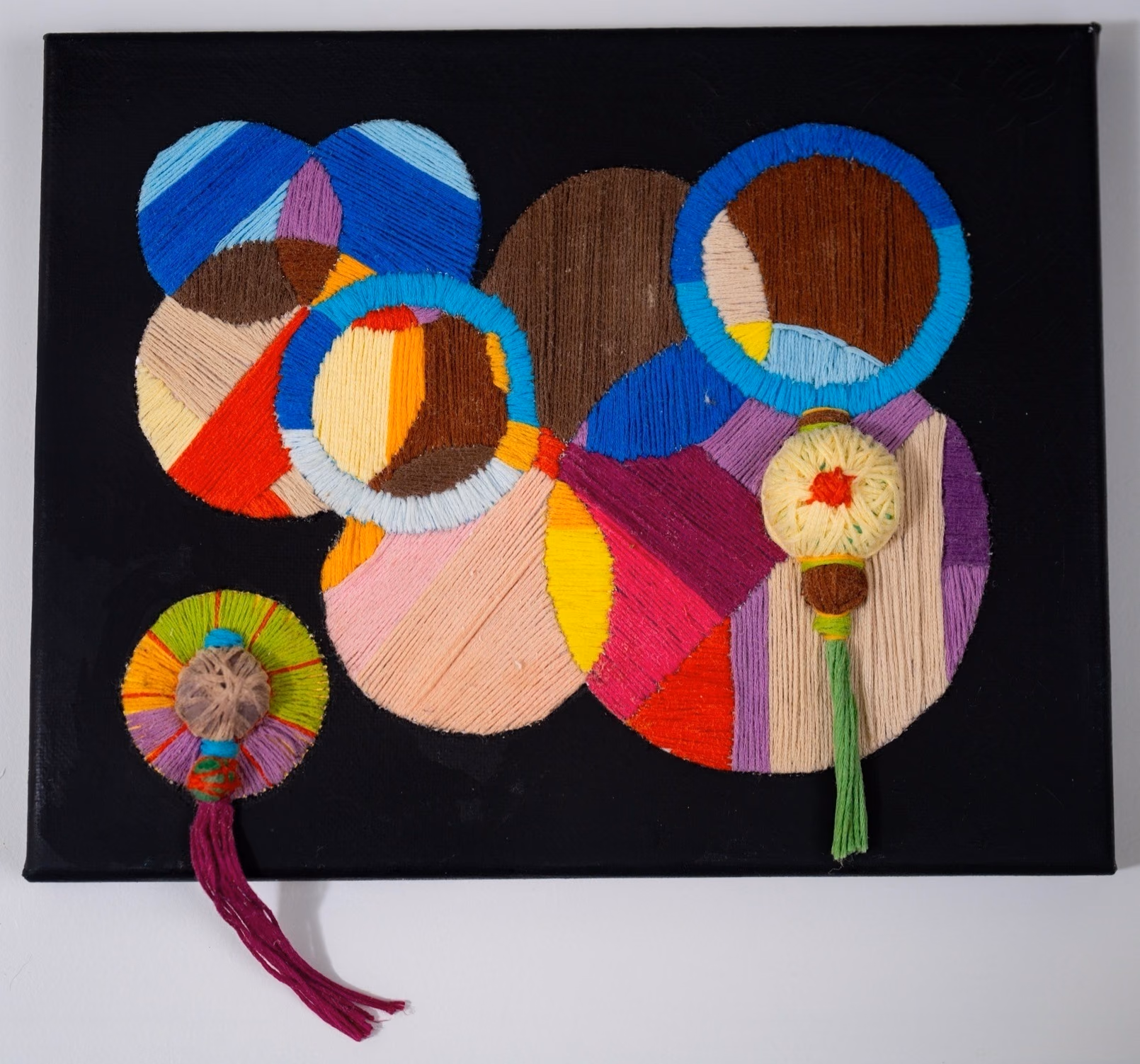 Thread on Black I by Victoria Zeder: vibrant thread work on black canvas, woven circles with dimensional yarn and tassel